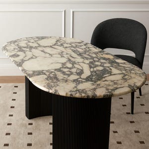 Puede incluir: Mesa ovalada con tapa de m&aacute;rmol y base negra acanalada. La encimera presenta un patr&oacute;n veteado crema y gris. Una silla gris oscuro est&aacute; colocada detr&aacute;s de la mesa. La mesa mide aproximadamente 152 cm de largo y 76 cm de ancho.