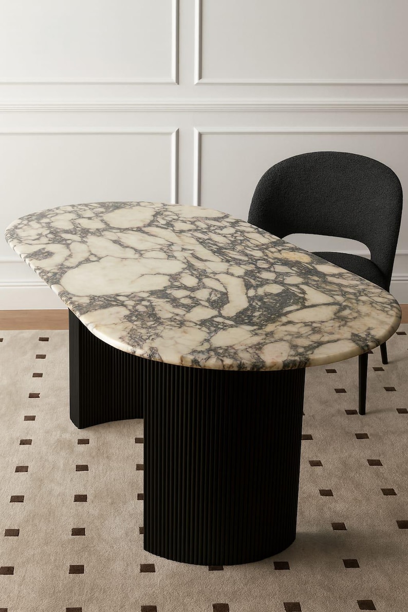 Puede incluir: Mesa ovalada con tapa de m&aacute;rmol y base negra acanalada. La encimera presenta un patr&oacute;n veteado crema y gris. Una silla gris oscuro est&aacute; colocada detr&aacute;s de la mesa. La mesa mide aproximadamente 152 cm de largo y 76 cm de ancho.
