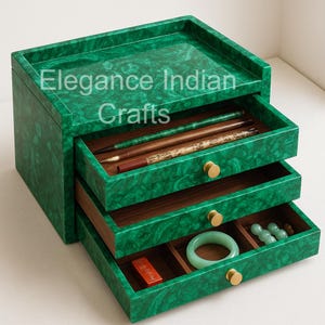 Może przedstawiać: Zielone pudełko na biżuterię w stylu malachitu z trzema szufladami, każda wyłożona ciemnym drewnem. Górna szuflada jest otwarta, ukazując długopisy. Dolna szuflada zawiera bransoletkę z jadeitu, koraliki i małe czerwone pudełko. Na górze widnieje napis "Elegance Indian Crafts".