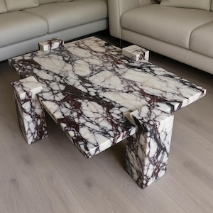 May include: A rectangular coffee table with a white and burgundy marble top and matching block legs. The table has a modern design and is placed in front of a white sofa.