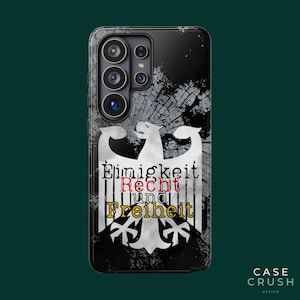 Könnte beinhalten: Eine schwarze Smartphone-Hülle mit einer weißen Adlergrafik in Used-Optik. Der Text "Einigkeit", "Recht" in Rot und "und Freiheit" in Gelb ist über den Adler gedruckt. Die Hülle hat einen Ausschnitt für eine Kamera mit mehreren Linsen.