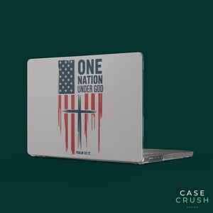 Könnte beinhalten: Ein hellgrauer Laptop-Aufkleber mit einer stilisierten amerikanischen Flagge mit vertikalen roten Streifen und einem blauen Sternenfeld. Darüber befindet sich ein dunkelblaues Kreuz und der Text ONE NATION UNDER GOD mit PSALM 33.12.