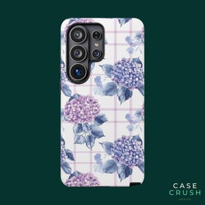 May include: A rectangular smartphone case featuring a white background with a light purple grid pattern. The design is decorated with clusters of blue and purple hydrangea flowers and green leaves. The camera cutout is located in the top left corner.