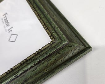 May include: Close-up of a green picture frame with a distressed finish. The frame has a textured surface and decorative detailing along the edges. The text "Frame It" is visible in the upper left corner.