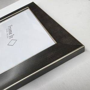 May include: Close-up of a dark brown picture frame with a silver inner edge. The frame has a textured wood grain appearance. The text "Frame It" is visible on the white background.