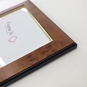 May include: Close-up of a wooden picture frame with a black border and gold inner trim. The frame has a natural wood grain pattern. The text "Frame It" is visible on the white background.