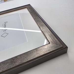 May include: A rectangular picture frame with a silver and brown textured border. The frame has a white mat and clear glass. The text "Frame It" is visible on the white mat.