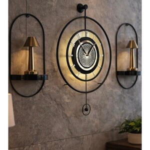 Puede incluir: Un reloj de pared decorativo con marco de metal negro y esfera dorada. Dos apliques a juego con lámparas doradas a cada lado. El reloj y los apliques están montados en una pared gris texturizada.