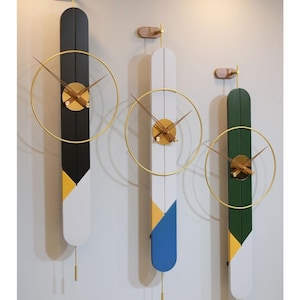 Könnte beinhalten: Drei moderne Wanduhren mit minimalistischem Design. Jede Uhr hat eine lange, vertikale Tafel in Schwarz, Weiß und Grün mit goldfarbenen Akzenten. Die Uhren haben einen kreisförmigen Goldrahmen und ein Pendel.