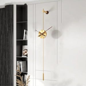 May include: A contemporary wall clock in gold. The clock has a circular face with simple hands and a long pendulum. It is mounted on a white wall, offering a minimalist design. The clock's design adds a touch of elegance to any room.