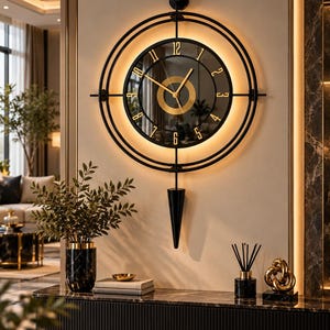 Puede incluir: Un reloj de pared circular con marco negro de doble anillo e iluminación LED cálida integrada. La esfera es negra con números y manecillas doradas, centrada por un anillo dorado. Un péndulo negro de forma puntiaguda cuelga en la parte inferior.