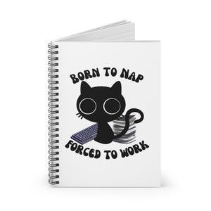 Pode incluir: Um caderno espiralado branco com uma ilustração de gato preto e o texto "BORN TO NAP FORCED TO WORK". O gato tem olhos grandes, um teclado e uma pilha de papéis.