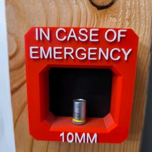 Könnte beinhalten: Rote Kunststoffbox mit den Worten „IN CASE OF EMERGENCY“ und „10MM“ in weißen Buchstaben. In der Box befindet sich ein silberner und gelber Steckschlüssel. Die Box ist auf einer Holzoberfläche montiert.