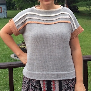 May include: A grey knitted short-sleeved top with a peach, white, and grey striped neckline.