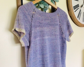 Puede incluir: Una blusa de punto de color morado con mangas cortas y un ribete blanco. La blusa tiene un escote redondo y un corte holgado.