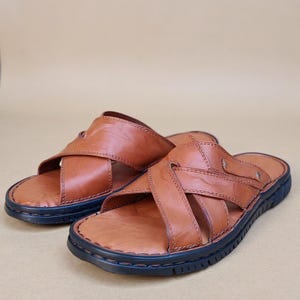 Puede incluir: Un par de sandalias de cuero marr&oacute;n con un dise&ntilde;o de correas entrecruzadas. Las sandalias tienen una suela azul oscuro y est&aacute;n hechas de cuero liso y texturizado. Las sandalias est&aacute;n dise&ntilde;adas para uso casual.