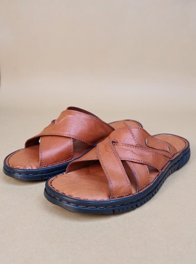 Puede incluir: Un par de sandalias de cuero marr&oacute;n con un dise&ntilde;o de correas entrecruzadas. Las sandalias tienen una suela azul oscuro y est&aacute;n hechas de cuero liso y texturizado. Las sandalias est&aacute;n dise&ntilde;adas para uso casual.