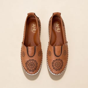 Top view of handmade tan leather slip-on flats for women with floral cutout detailing, soft leather finish, and clean slip-on silhouette.