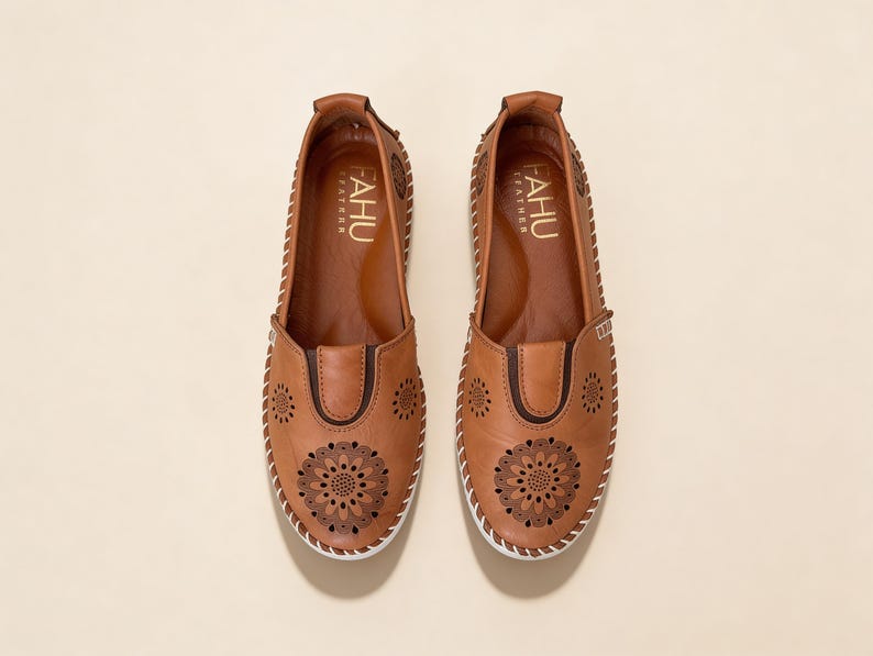 Top view of handmade tan leather slip-on flats for women with floral cutout detailing, soft leather finish, and clean slip-on silhouette.