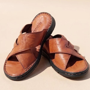 Puede incluir: Un par de sandalias de cuero marr&oacute;n con un dise&ntilde;o entrecruzado. Las sandalias tienen una suela negra y una parte superior de cuero texturizado. La marca "ecco" es visible en la plantilla. Las sandalias est&aacute;n dise&ntilde;adas para la comodidad y el uso informal.