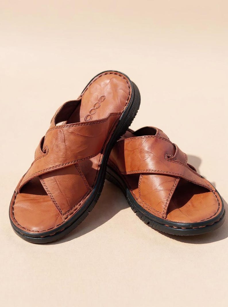 Puede incluir: Un par de sandalias de cuero marr&oacute;n con un dise&ntilde;o entrecruzado. Las sandalias tienen una suela negra y una parte superior de cuero texturizado. La marca "ecco" es visible en la plantilla. Las sandalias est&aacute;n dise&ntilde;adas para la comodidad y el uso informal.