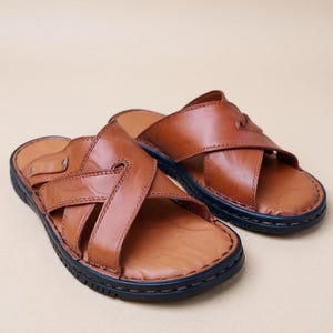Puede incluir: Un par de sandalias de cuero marr&oacute;n con un dise&ntilde;o de correas cruzadas. Las sandalias tienen una suela azul oscuro y est&aacute;n hechas de cuero liso de alta calidad. Las sandalias est&aacute;n dise&ntilde;adas para la comodidad y el estilo.