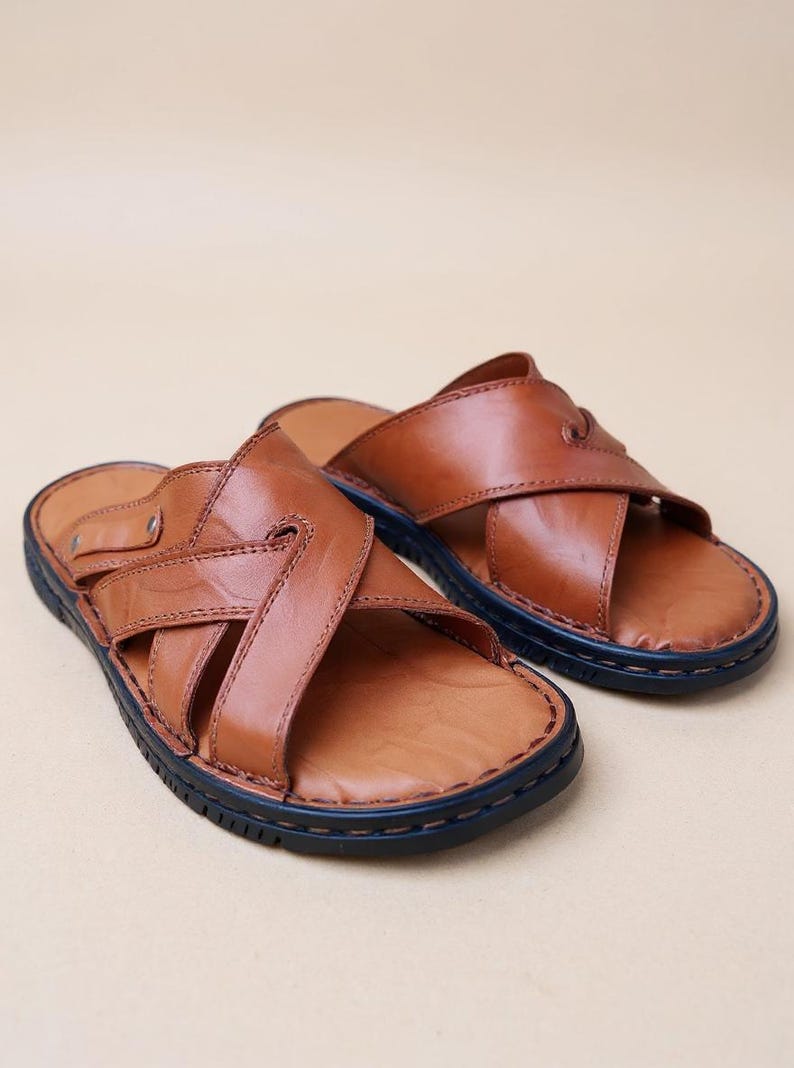 Puede incluir: Un par de sandalias de cuero marr&oacute;n con un dise&ntilde;o de correas cruzadas. Las sandalias tienen una suela azul oscuro y est&aacute;n hechas de cuero liso de alta calidad. Las sandalias est&aacute;n dise&ntilde;adas para la comodidad y el estilo.