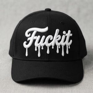 May include: A black baseball cap featuring white embroidered text that reads "Fuckit" in a cursive script font. The lettering has a distinct dripping effect, with white embroidery extending downward from the base of each letter onto the cap crown.