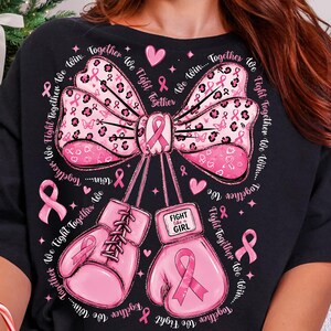 May include: A black t-shirt featuring a large pink bow with a leopard print pattern and small pink ribbons. Below the bow are two pink boxing gloves, one with the text "FIGHT like a GIRL". The design includes the repeated text "Together We Fight Together We Win".