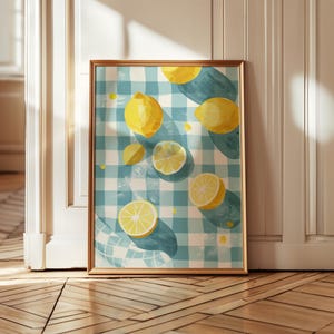 Könnte beinhalten: Ein gerahmter Kunstdruck mit einer Aquarellillustration von Zitronen auf einer blau-weiß karierten Tischdecke. Die Zitronen sind ganz und geschnitten, mit gelben und weißen Farbtönen. Der Rahmen ist goldfarben.
