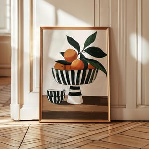 Könnte beinhalten: Gerahmter Kunstdruck mit einem Stillleben von Orangen in einer schwarz-weiß gestreiften Schale mit Sockel. Grüne Blätter und eine kleine Schale mit passenden Streifen sind ebenfalls abgebildet. Das Kunstwerk ist vor einem neutralen Hintergrund.