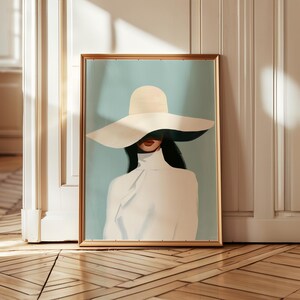 Könnte beinhalten: Gerahmter Kunstdruck mit einer Frau in weißem Hut und Oberteil. Das Kunstwerk hat einen hellblauen Hintergrund und einen goldenen Rahmen. Das Gesicht der Frau ist teilweise vom Hut verdeckt, nur ihre roten Lippen sind sichtbar.