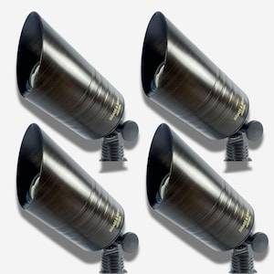 May include: Four bronze-colored outdoor spotlights with a cylindrical design. Each spotlight has a flared opening and a small adjustable knob. The brand name "Brass & Beam" is printed on each spotlight.
