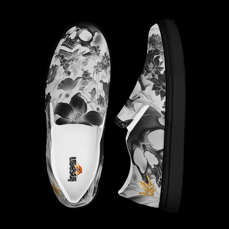 May include: A pair of slip-on sneakers featuring a black and white graphic print of a human skull surrounded by various flowers. The interior of the shoe displays a small logo with the text "LUSIT" and a gold origami crane icon.