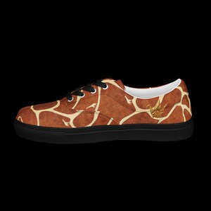 May include: A low-top sneaker featuring a brown and cream giraffe-inspired pattern across the upper. The shoe has black laces, a white interior lining, and a solid black rubber sole. A small gold-colored crane icon is visible on the side.