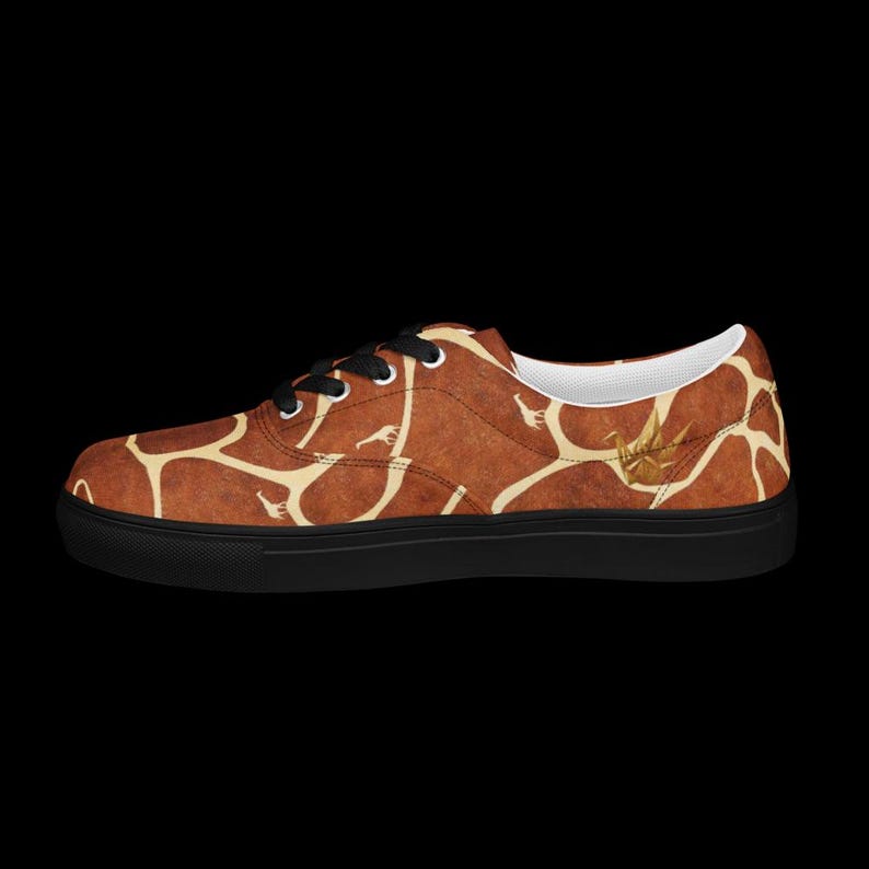 May include: A low-top sneaker featuring a brown and cream giraffe-inspired pattern across the upper. The shoe has black laces, a white interior lining, and a solid black rubber sole. A small gold-colored crane icon is visible on the side.
