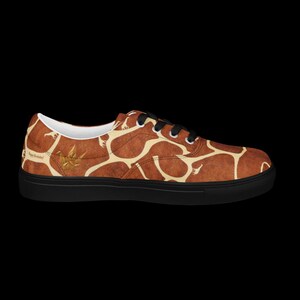 May include: A low-top sneaker featuring a brown and cream giraffe-inspired pattern across the upper. The shoe has black laces, a black sole, and a small gold-colored origami crane graphic near the heel with the text Happy Birthday printed.