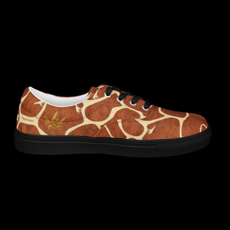 May include: A low-top sneaker featuring a brown and cream giraffe-inspired pattern across the upper. The shoe has black laces, a black sole, and a small gold-colored origami crane graphic near the heel with the text Happy Birthday printed.