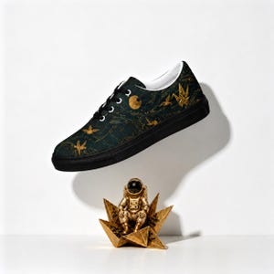 May include: A low-top sneaker with a dark green and black marbled pattern featuring gold-colored bird silhouettes and a circular moon graphic. Below the shoe sits a small gold-colored astronaut figurine perched on a geometric star-shaped base.