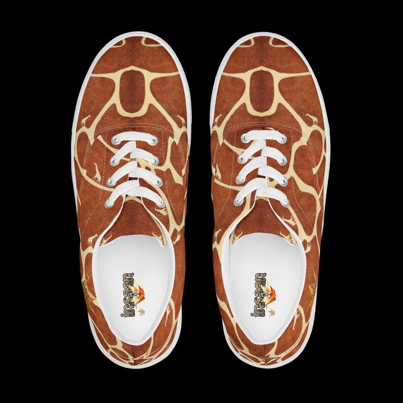 May include: A pair of low-top sneakers featuring a brown and cream giraffe print pattern across the exterior. The shoes have white laces, white rubber soles, and white interior linings with the text "insaan" printed on the heel of the insole.