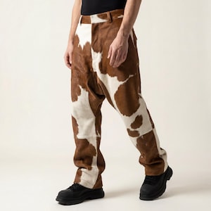 May include: Brown and white cowhide patterned trousers. The trousers have a relaxed fit and a classic five-pocket design. The model is wearing black shoes.