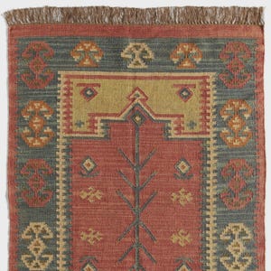 May include: A rectangular rug with a red central field and a blue border. The rug features geometric patterns in yellow, orange, and blue. The top edge has a brown fringe.
