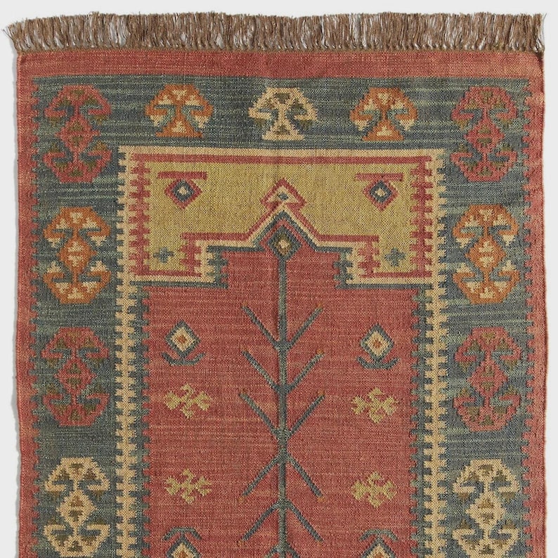 May include: A rectangular rug with a red central field and a blue border. The rug features geometric patterns in yellow, orange, and blue. The top edge has a brown fringe.