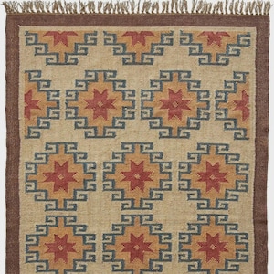 May include: A rectangular jute rug with a geometric pattern. The design features repeating diamond shapes with starburst centers in red and gold, framed by blue squares. The rug has a brown border and fringe.