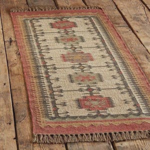 May include: Rectangular area rug with a beige central field and a geometric pattern in red, gray, and brown. The rug has a red border with fringe on the short ends. The rug is made of natural fibers.