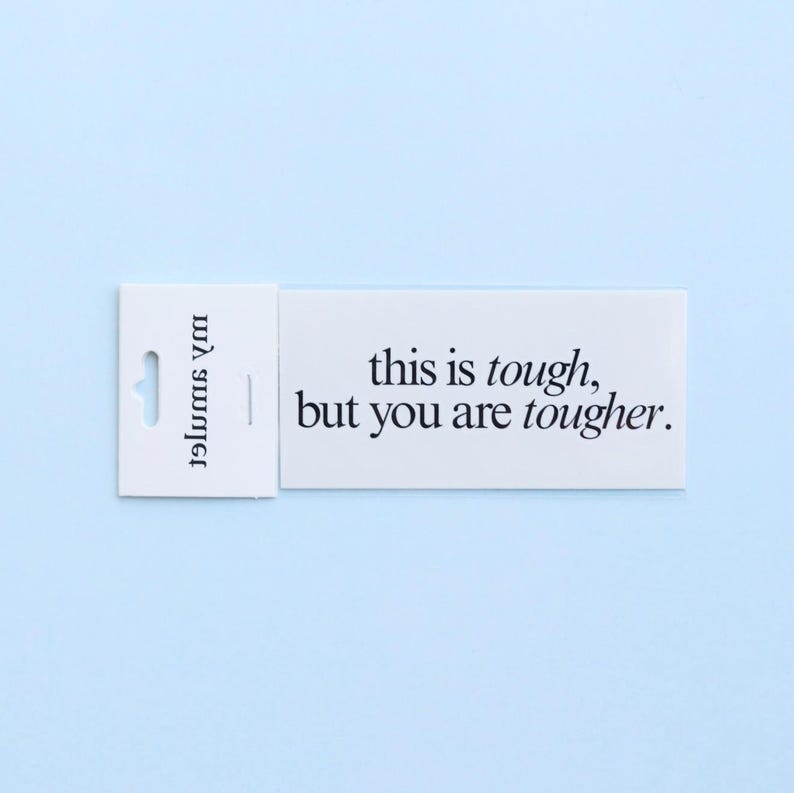 May include: A white rectangular tag with the text "this is tough, but you are tougher" in black. The tag has a small hole for hanging and the words "my summer" printed vertically on the left side. The background is a light blue.
