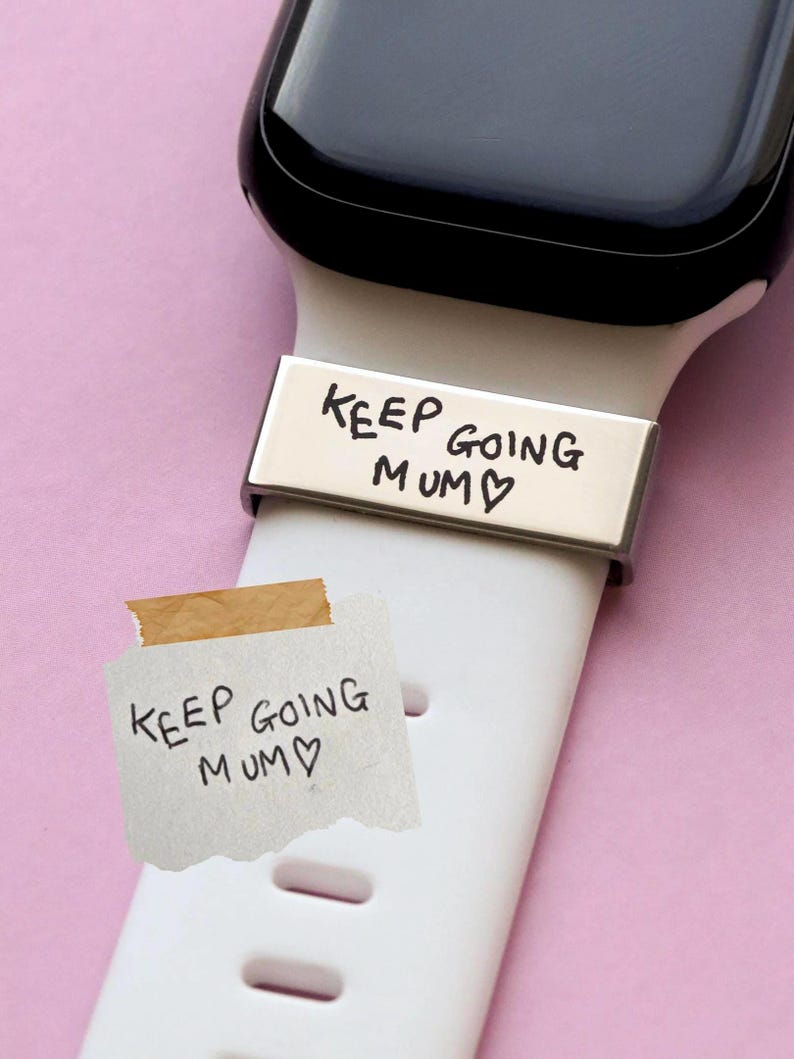 May include: A silver watch band with the words "KEEP GOING MUM" engraved on it. A small piece of paper with the same message is taped to the white watch band. The watch face is black.