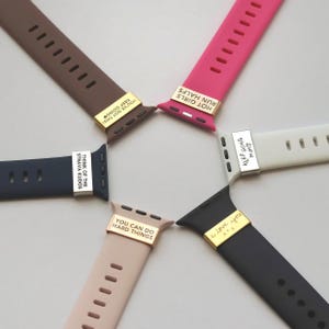May include: A collection of colorful watch bands in brown, pink, navy, beige, black, and white. Each band features a gold-colored metal accent with an inspirational phrase such as "You've Got This!" or "I Love You" in black text.
