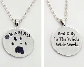 以下が含まれることがあります： 片側に肉球の跡と「RAMBO」という名前、もう片側に「Best Kitty In The Whole Wide World」という文字が刻まれた丸いペンダントが付いたシルバーネックレスです。