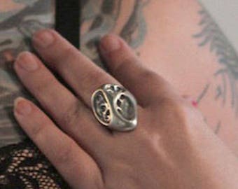 May include: A silver ring with an intricate design. The ring is worn on the finger of a person with a tattoo on their arm.